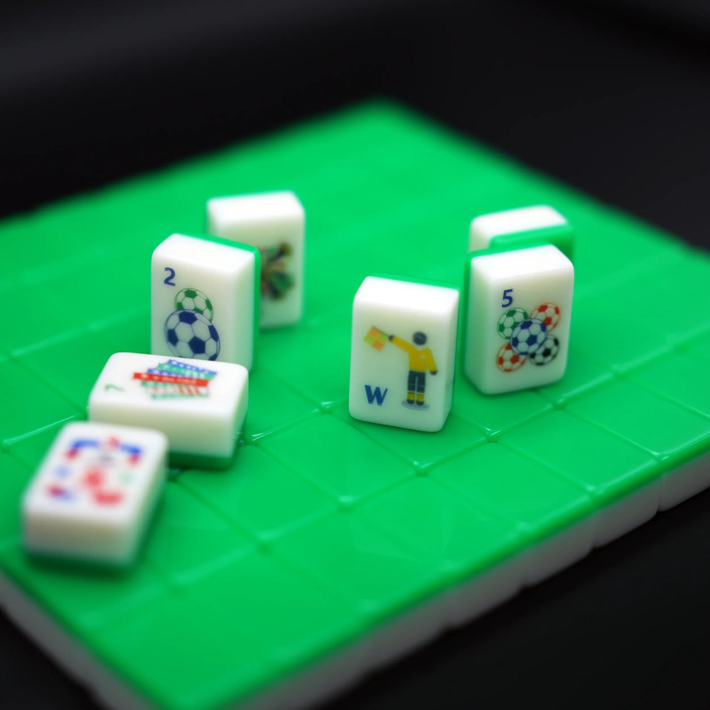 Selective focus shot of soccer ball dot and yellow referee wind Mahjong tiles standing upright on a textured green mat.