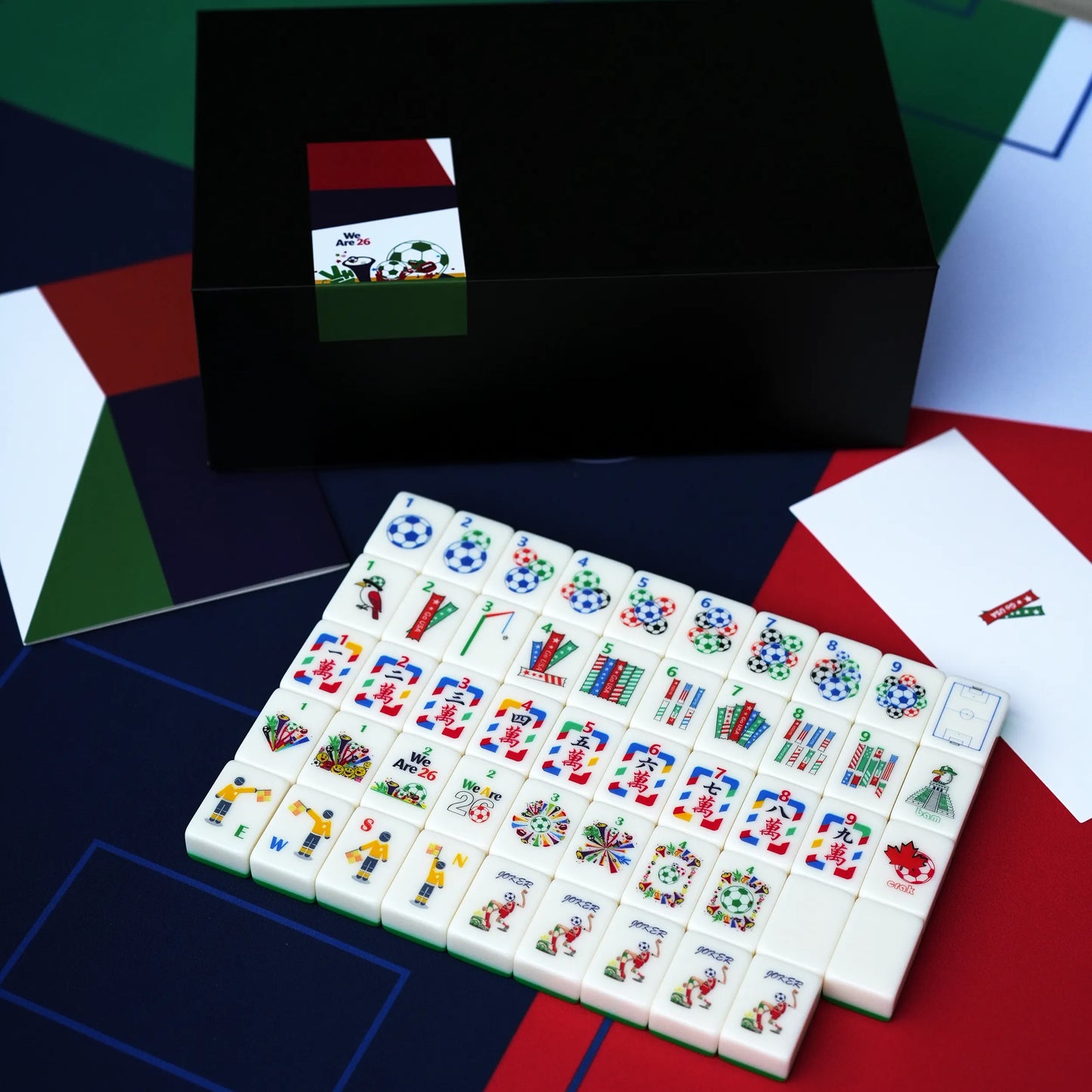 The soccer championship American Mahjong tile block displayed next to its matte black storage box on a multi-colored field mat.