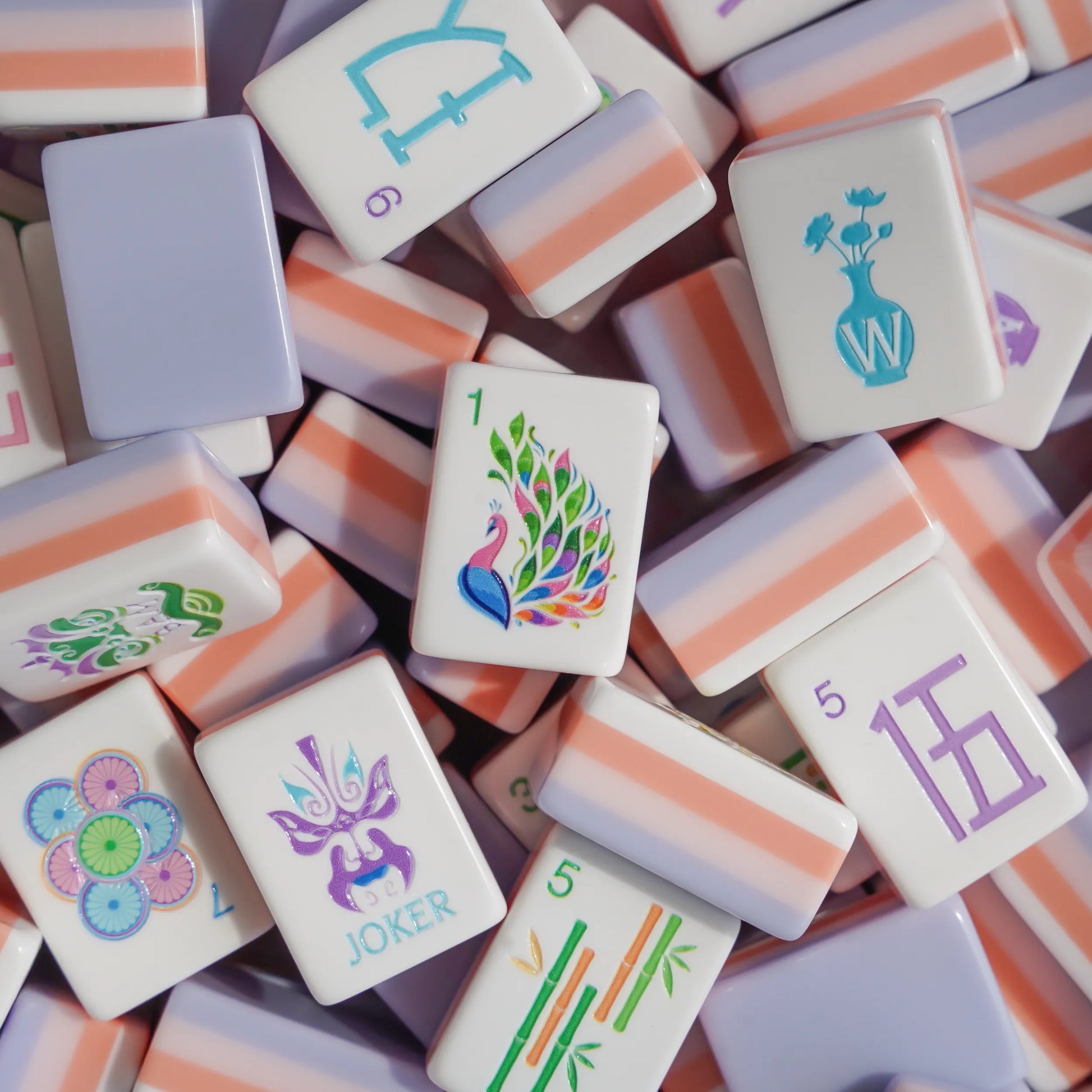 A close-up jumbled view of the Opera Mask Heritage American Mahjong tiles, showcasing the solid peach and lilac multi-layer core next to hand-painted opera mask jokers.