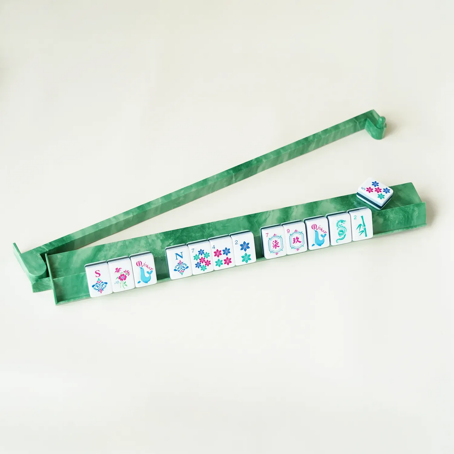 A single jade green mahjong rack holding a neat row of American mahjong tiles with the pusher extended, demonstrating game night play.