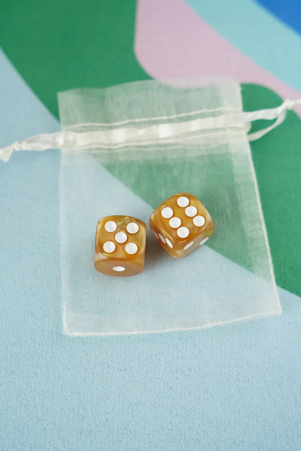 A pair of amber gold 5/8 inch marbled acrylic mahjong dice with white pips in a sheer organza pouch.