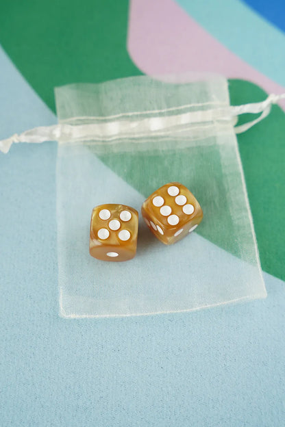 A pair of amber gold 5/8 inch marbled acrylic mahjong dice with white pips in a sheer organza pouch.