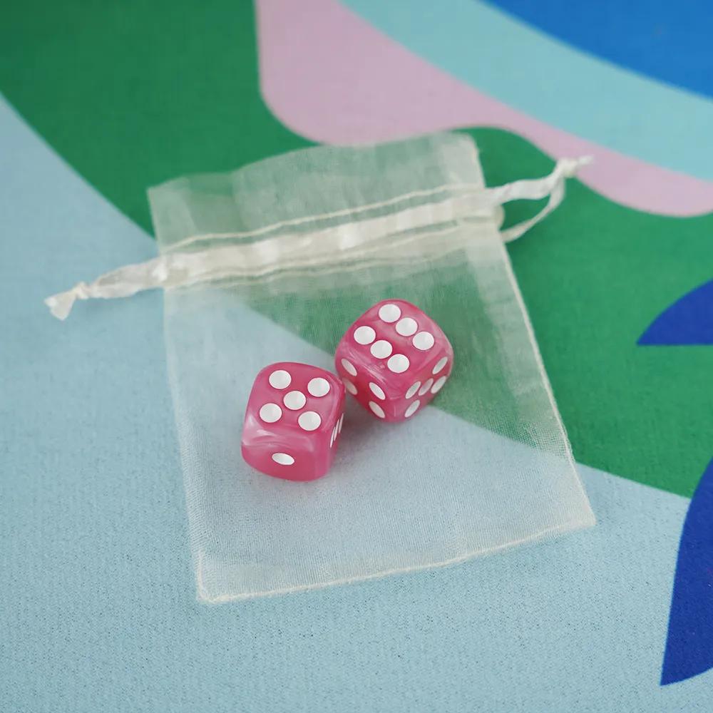 A pair of bubblegum pink marbled acrylic mahjong dice with high-contrast white pips in a sheer white organza pouch.