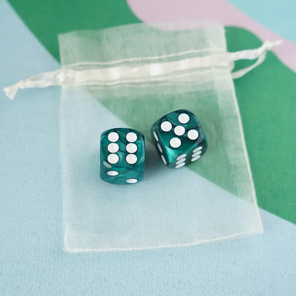 A pair of deep emerald teal marbled acrylic mahjong dice with crisp white pips in a sheer organza pouch.