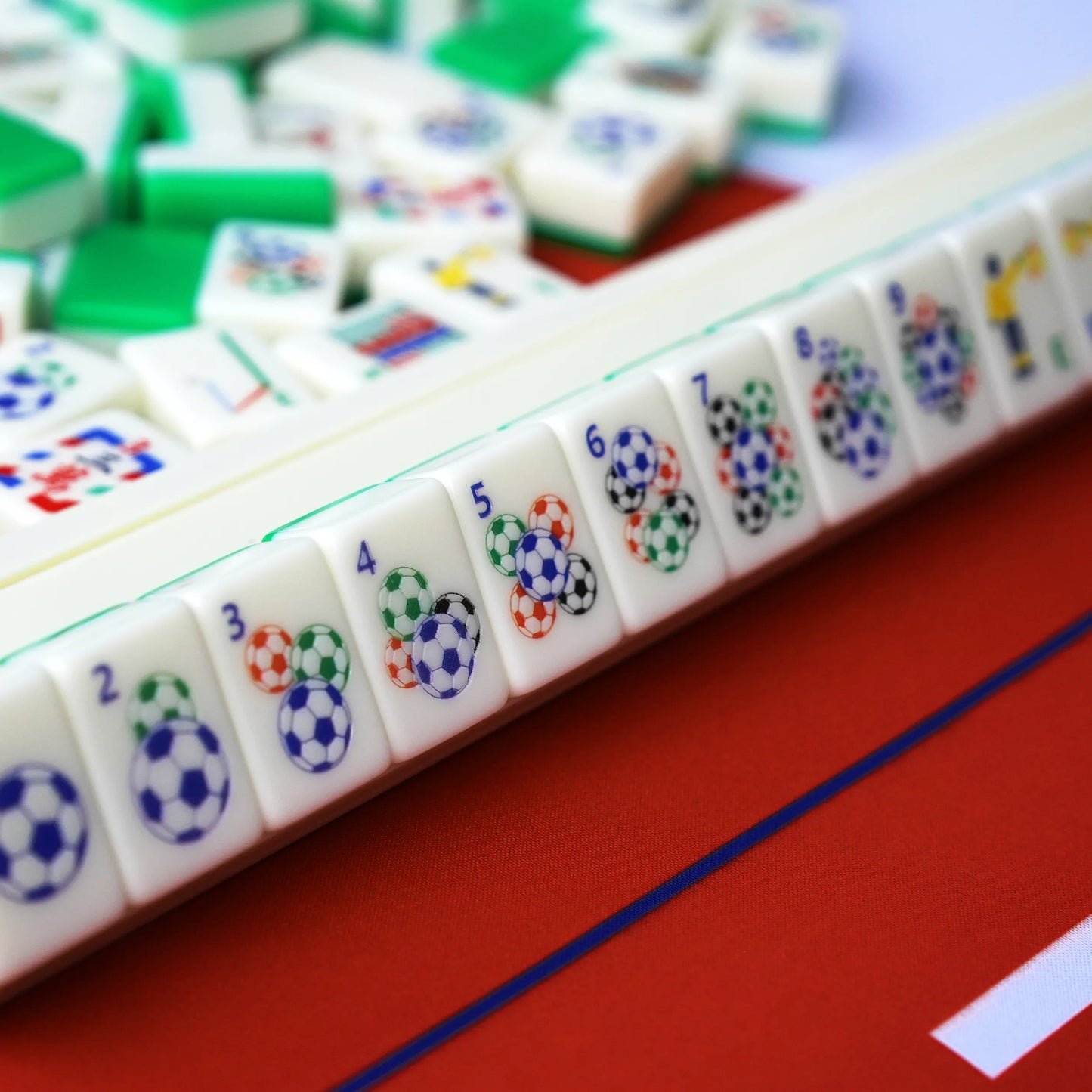 A close-up view of soccer ball numeric dot tiles lined up on a cream-colored American Mahjong rack over a red mat.